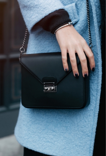 Thirds shot of model in blue coat with hand on purse and painted nails